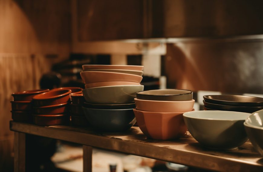 Stacks of colorful ceramic bowls on a wooden shelf.