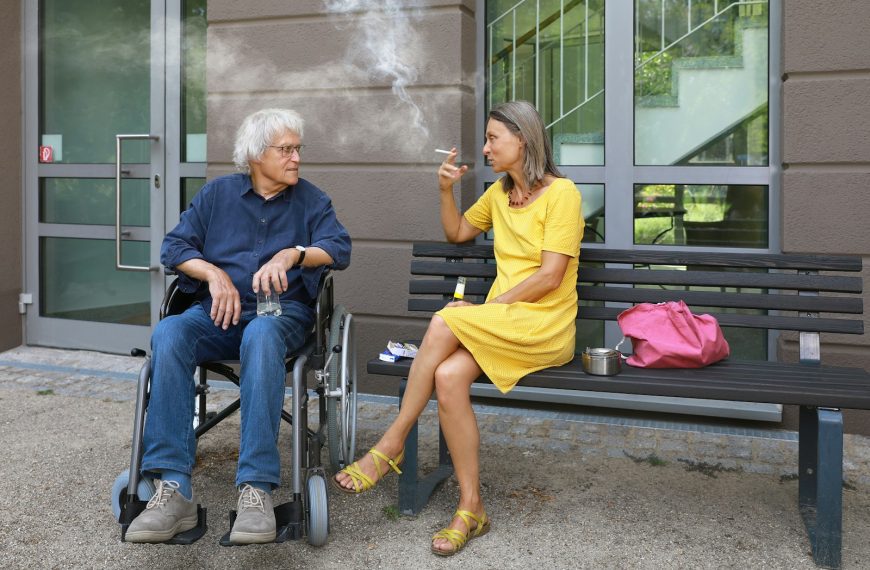 a man sitting on a bench next to a woman smoking a cigarette