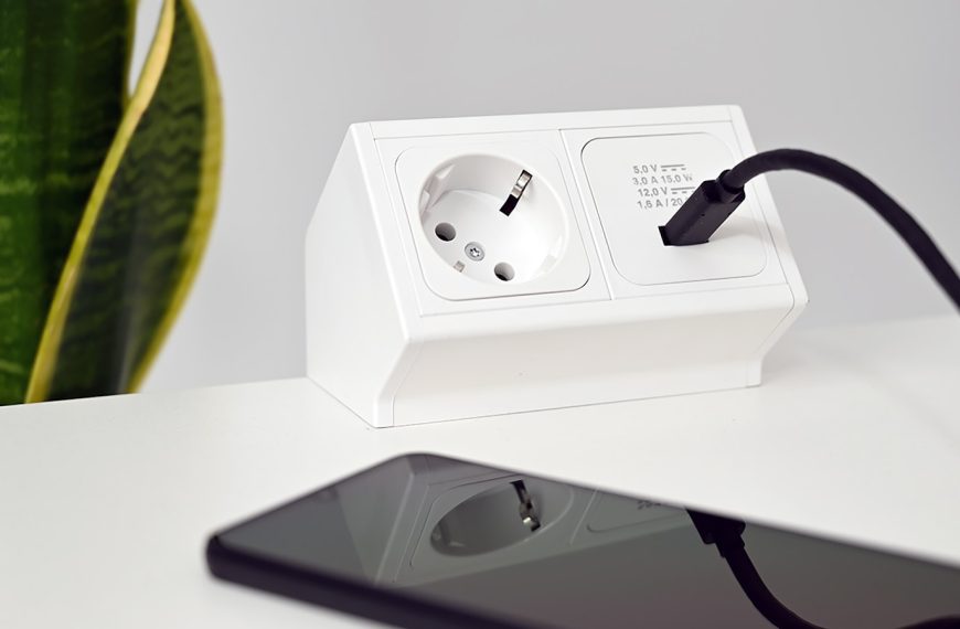 a phone charging on a white table next to a plant