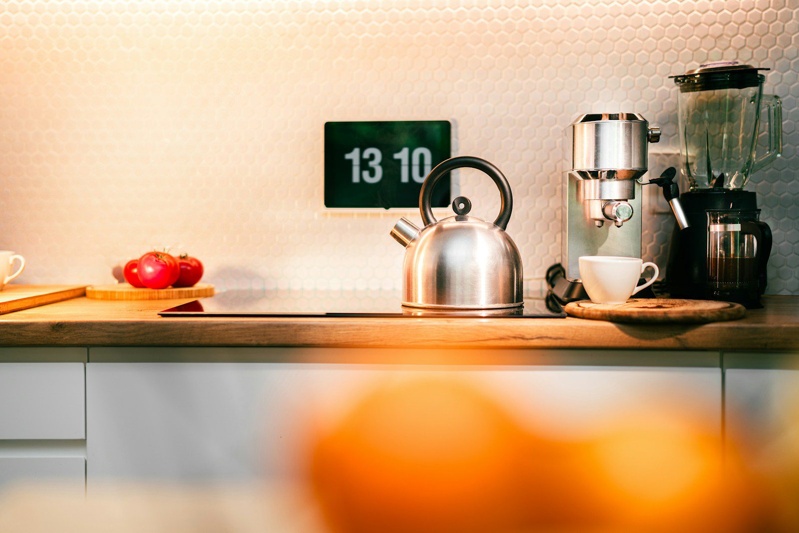 A kitchen counter with a tea kettle, oranges, and other kitchen items