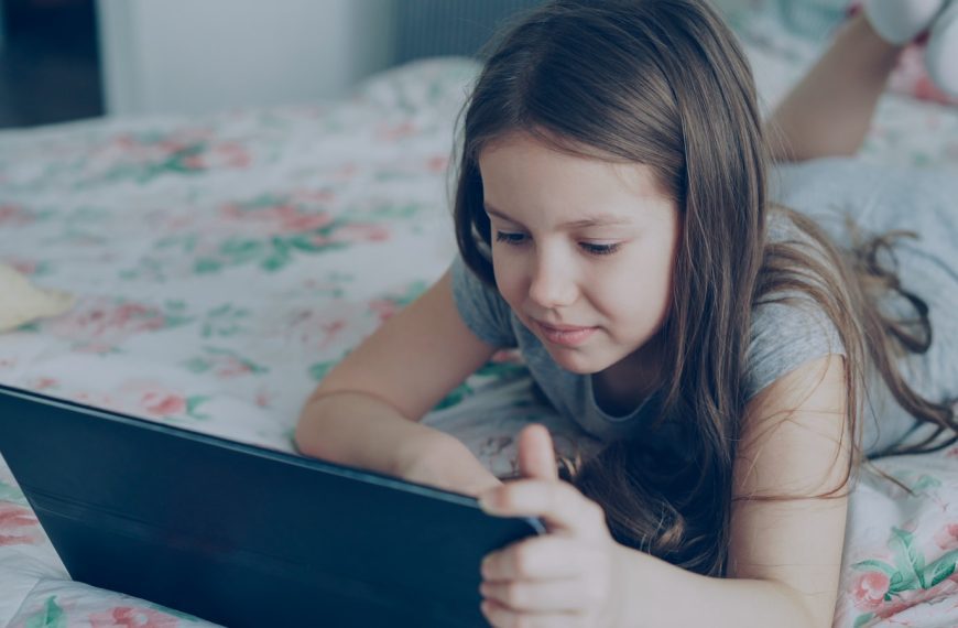 A girl is using a tablet on her bed.
