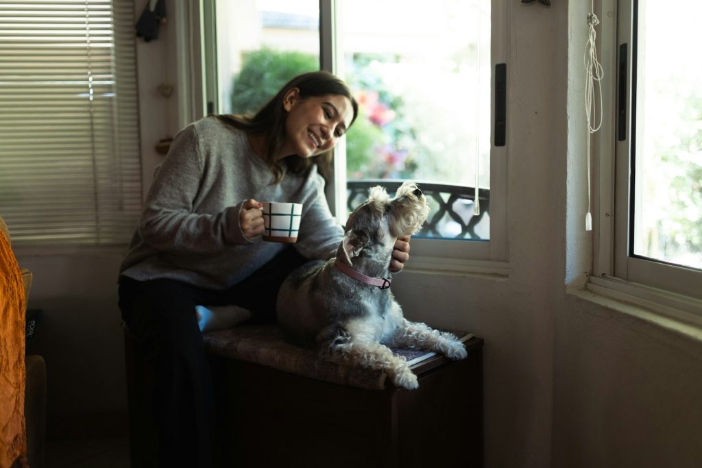 Woman holding coffee cup petting a dog by window
