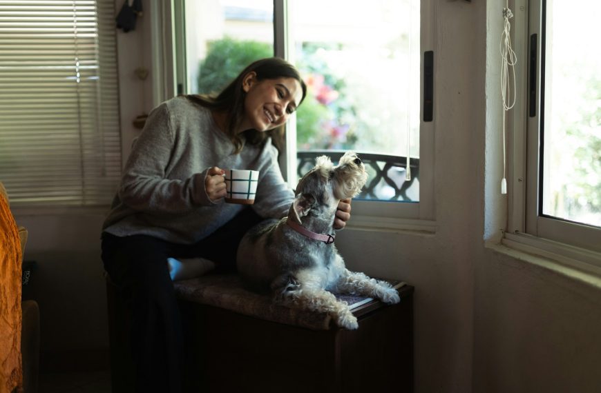 Woman holding coffee cup petting a dog by window