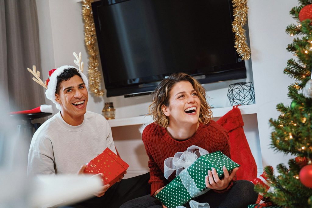 a person and a girl sitting on a couch with presents in front of a christmas tree