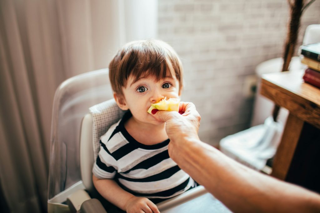 boy in black and white stripe shirt eating yellow fruit sitting on white sofa