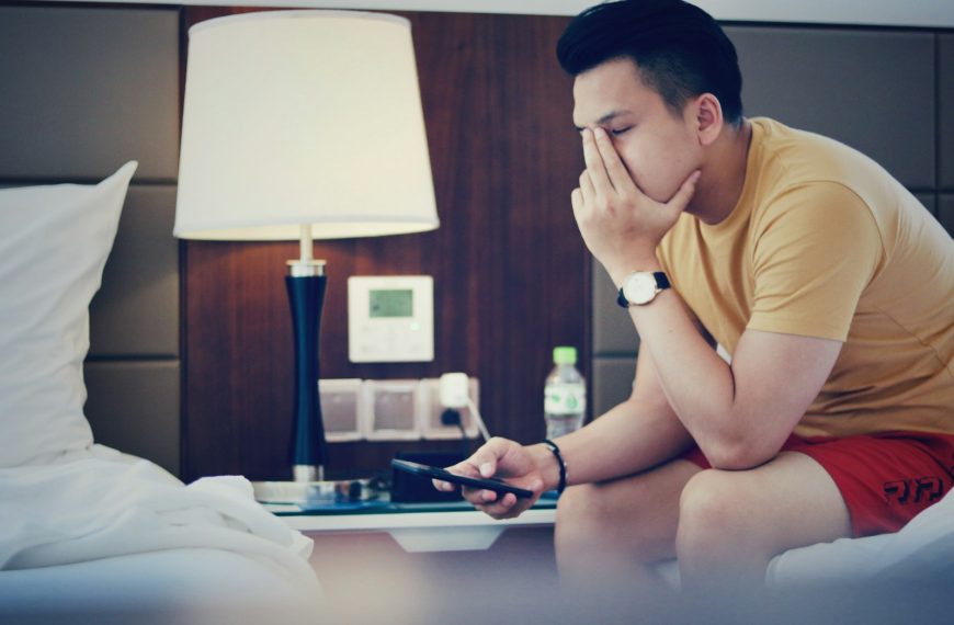 man holding phone and sitting while putting left hand on his face