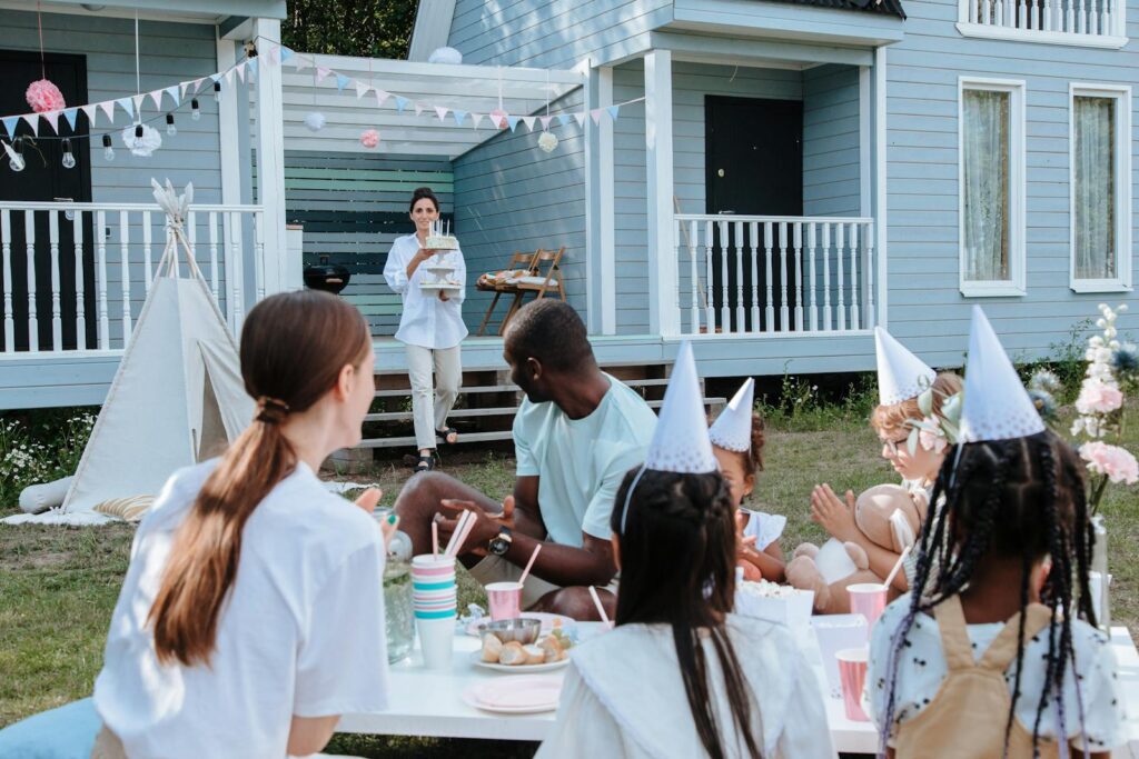 Children and adults celebrating a birthday outdoors with food and decorations.