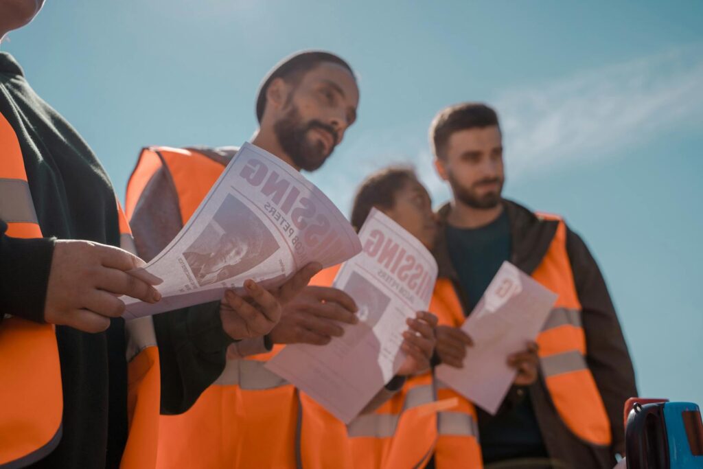 Group of volunteers in orange vests distributing missing person flyers outdoors.