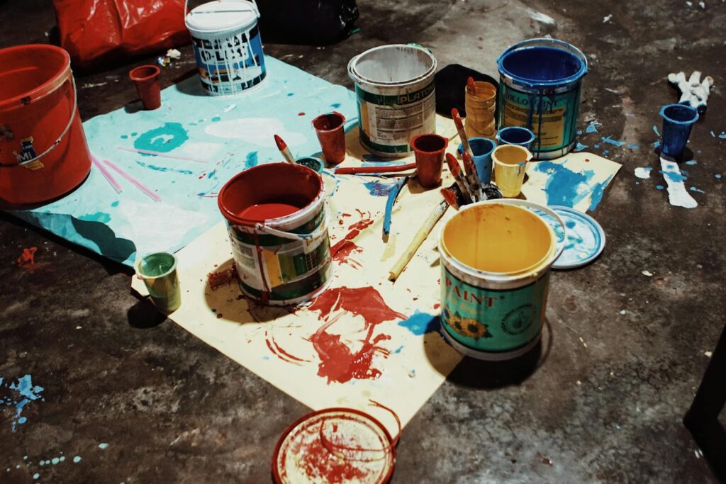 Artistic mess of various colored paint cans and brushes on a studio floor.