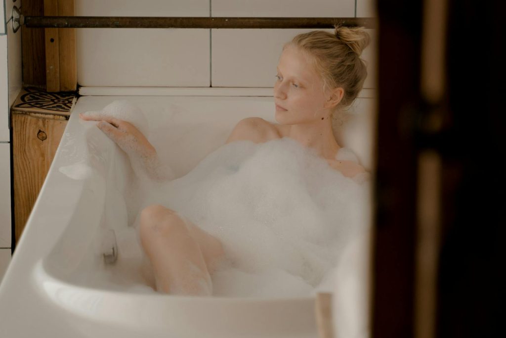 A serene moment of relaxation as a blond woman enjoys a bubble bath in a modern bathroom.