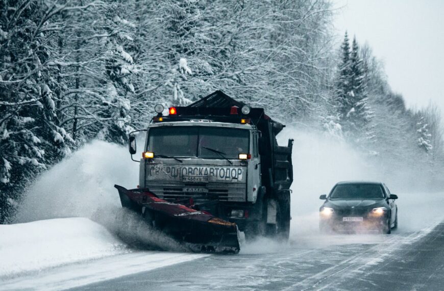 A snowplow clears a snowy road through a forest, enhancing winter driving safety.