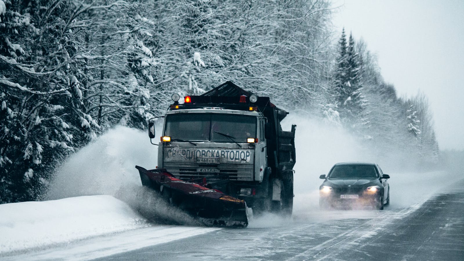 A snowplow clears a snowy road through a forest, enhancing winter driving safety.