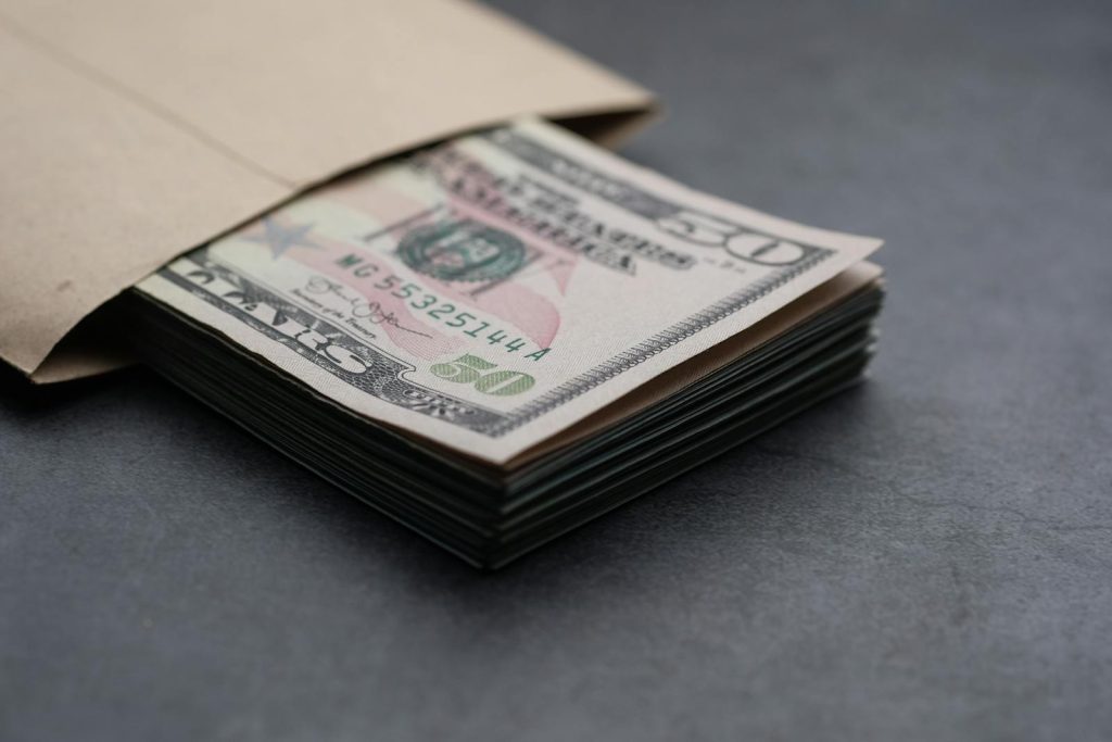 Close-up of US fifty dollar bills partially enclosed in a brown envelope, symbolizing finances.