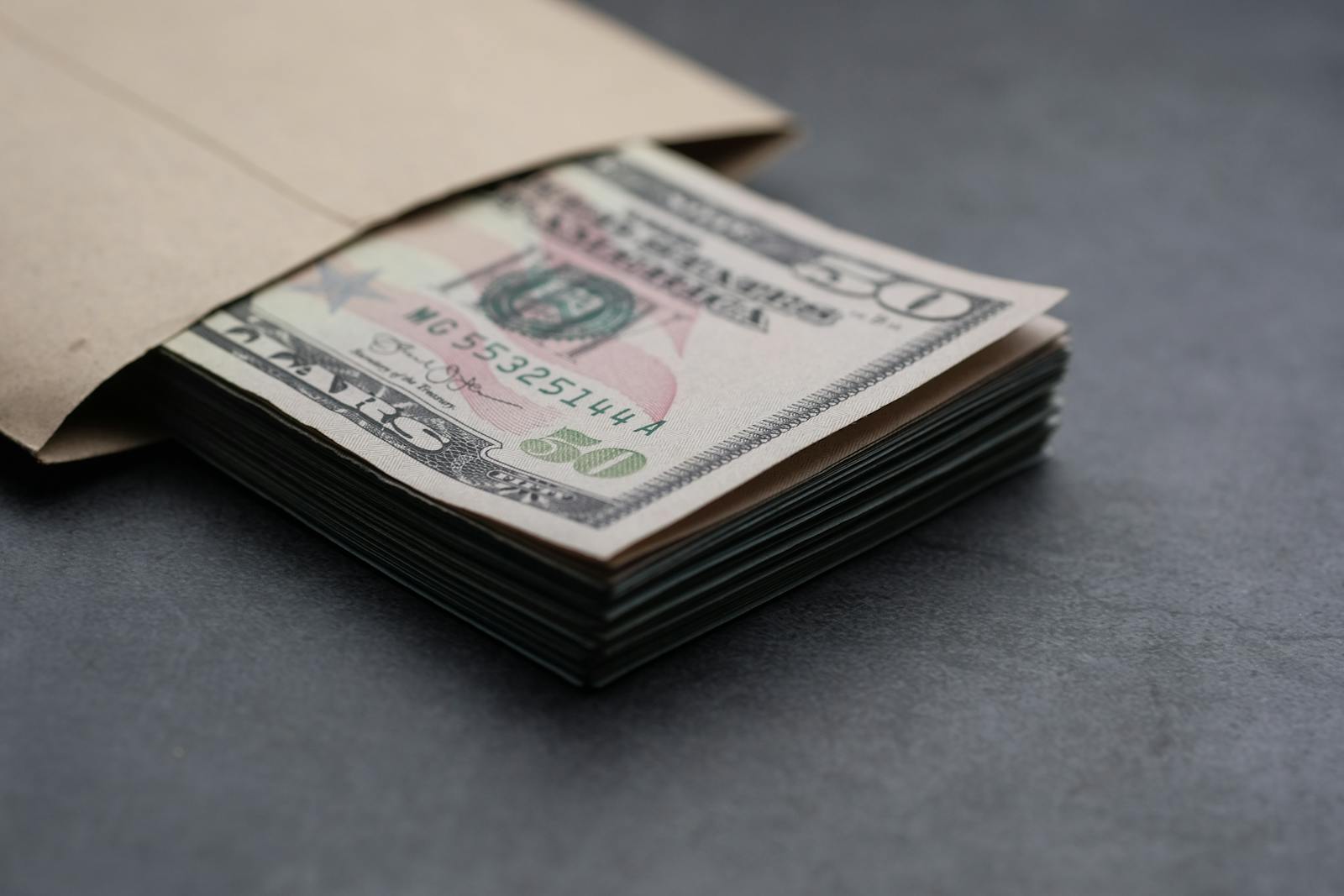 Close-up of US fifty dollar bills partially enclosed in a brown envelope, symbolizing finances.