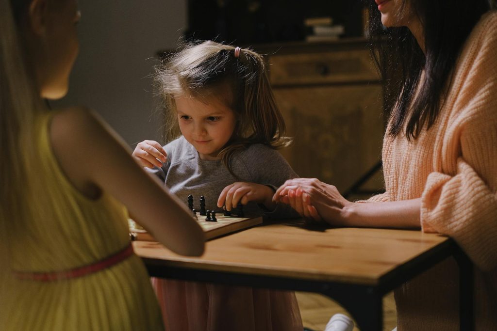 Mother and daughters enjoying a chess game indoors. Captures a heartwarming family moment.
