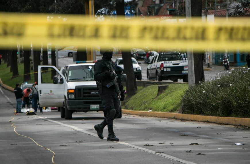 Police officers investigate and secure a crime scene in an urban street with caution tape.