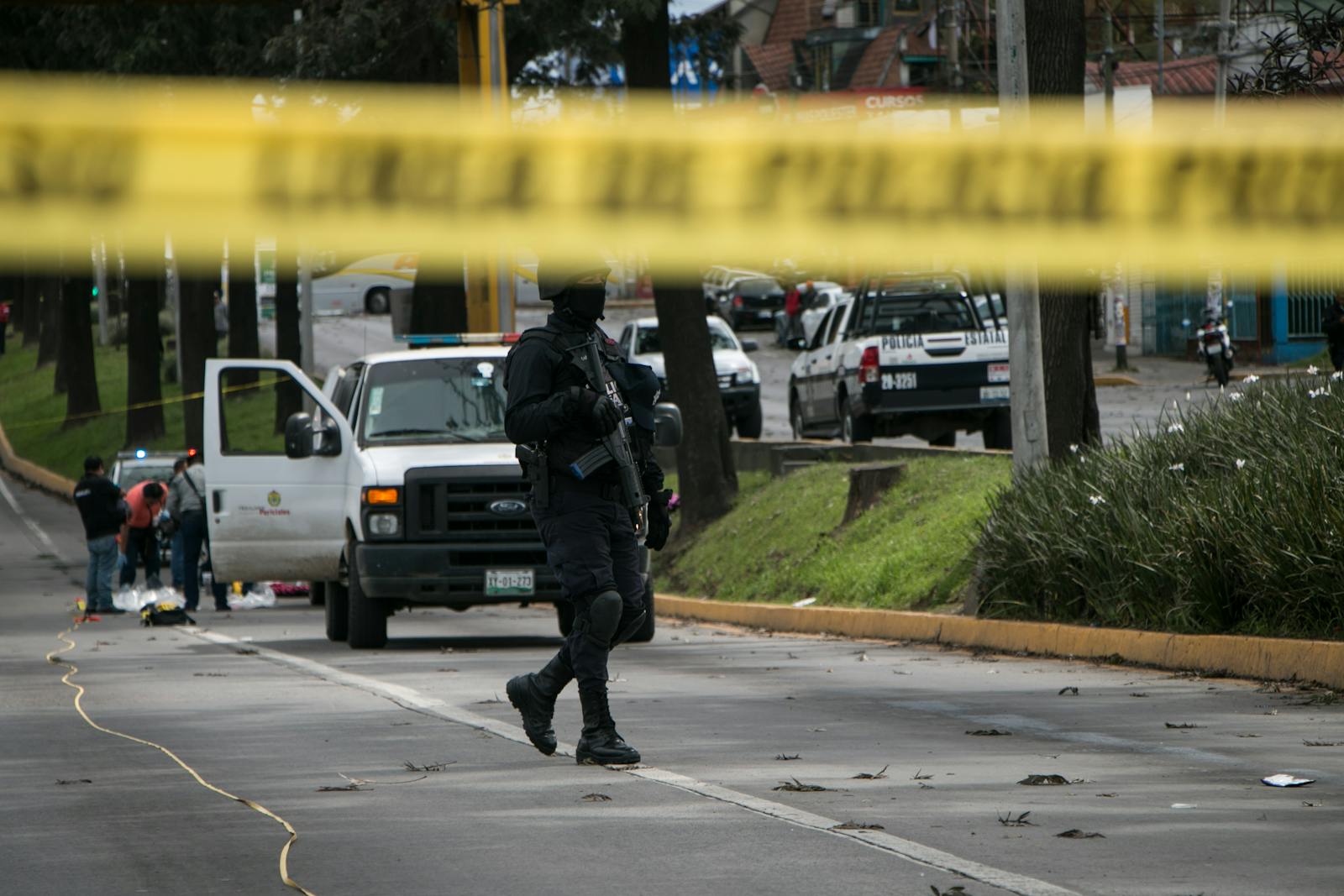 Police officers investigate and secure a crime scene in an urban street with caution tape.