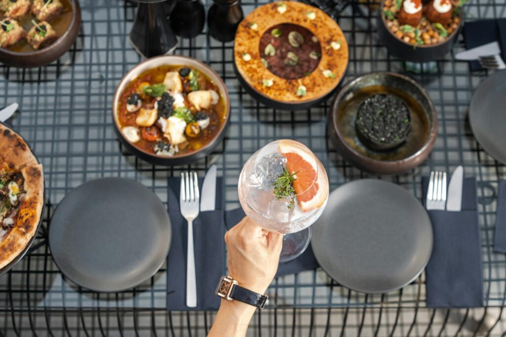 An overhead shot of an exquisite dining setting featuring gourmet dishes and a hand holding a refreshing beverage.