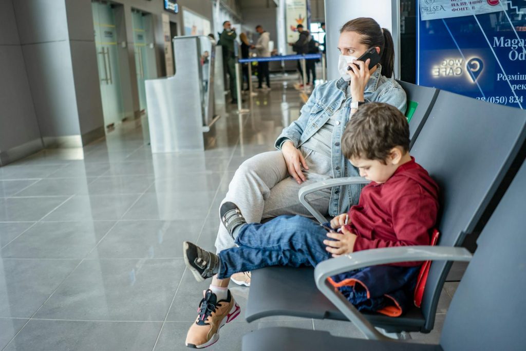 A mother and child sitting at an airport terminal. The mother is on the phone while the child is using a device.