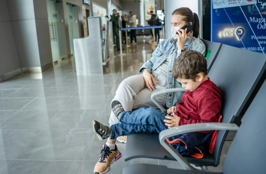 A mother and child sitting at an airport terminal. The mother is on the phone while the child is using a device.