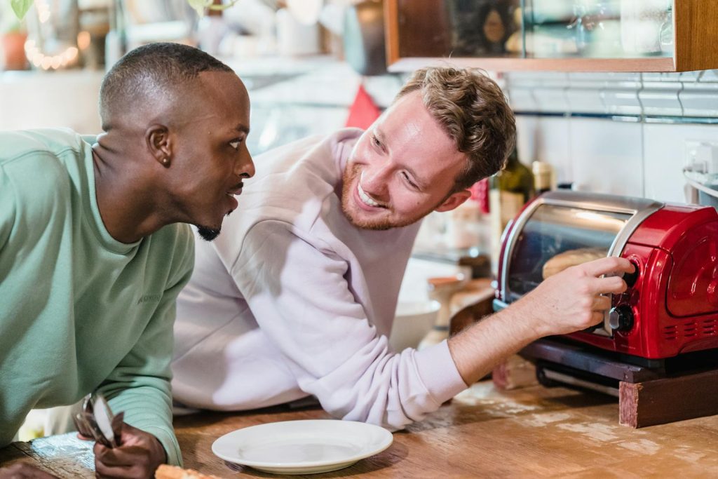Two men sharing a joyful morning in a kitchen, preparing breakfast with smiles.
