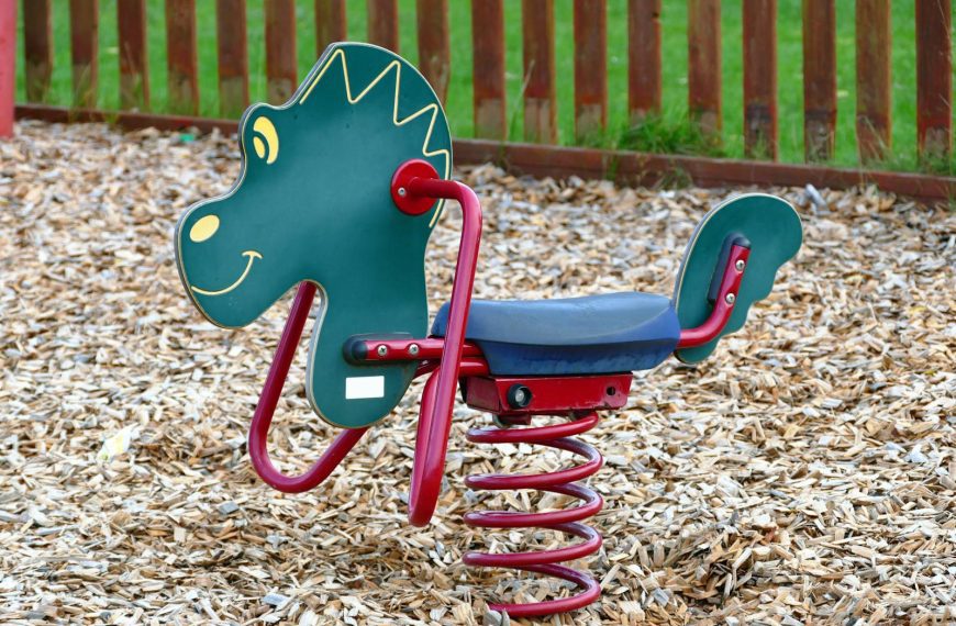 A colorful dinosaur-themed spring rider in an outdoor playground with wood chips.
