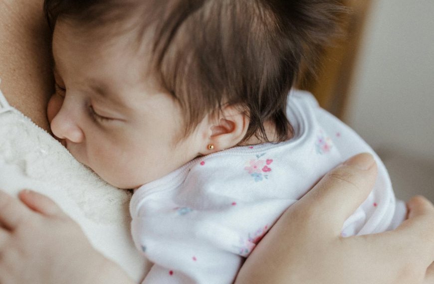 Close-up of a peaceful newborn sleeping, cradled gently in their mother's arms indoors.