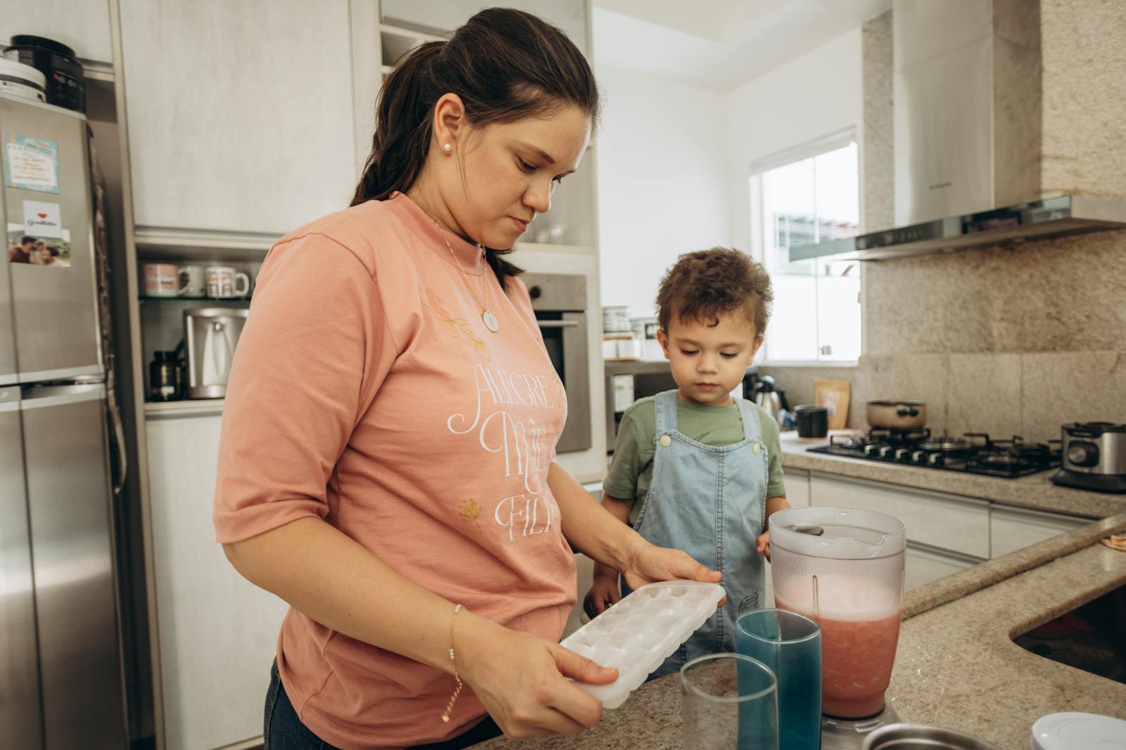 A woman and her son making a drink together in a modern kitchen.