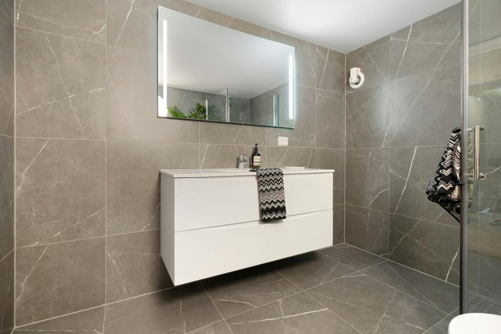 Elegant bathroom featuring a large mirror, modern vanity, and sleek grey tiled walls.