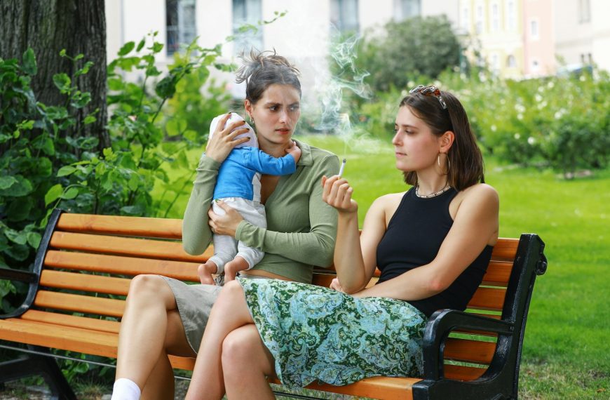 two women sitting on a park bench smoking a cigarette