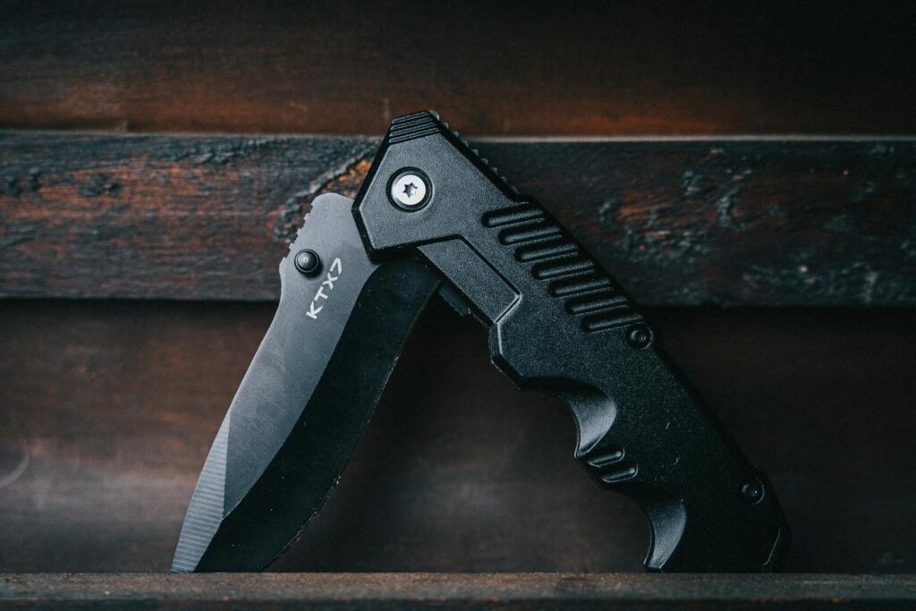 Close-up of a black folding knife on a wooden background, emphasizing its sharp blade.