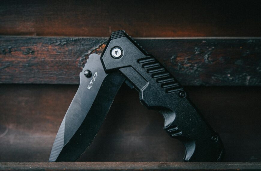 Close-up of a black folding knife on a wooden background, emphasizing its sharp blade.