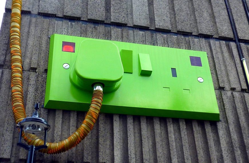 Low-angle view of a green electric outlet on a textured building wall.