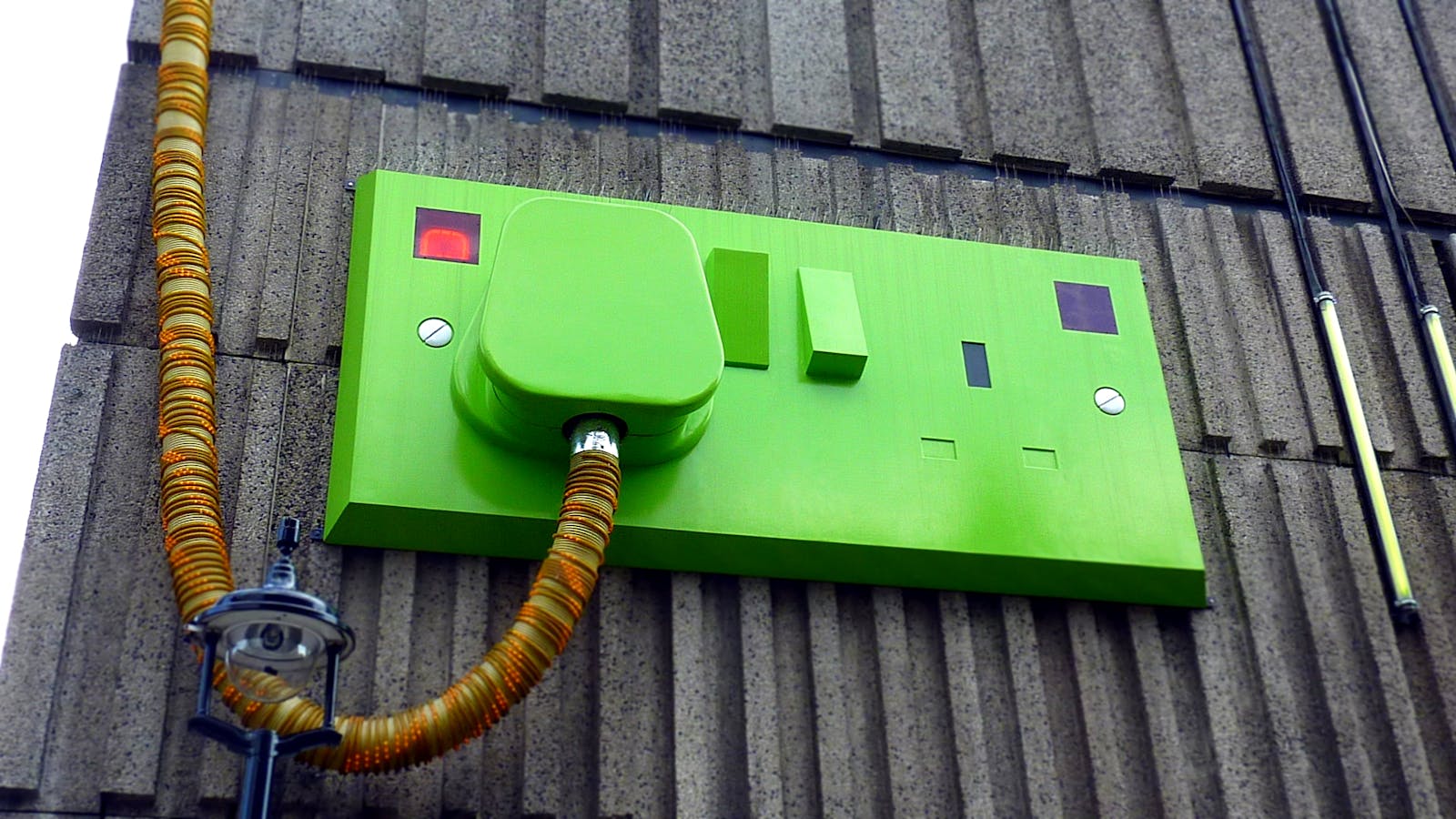Low-angle view of a green electric outlet on a textured building wall.