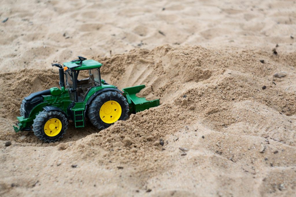 Green toy tractor in sand, symbolizing playful exploration and creativity.