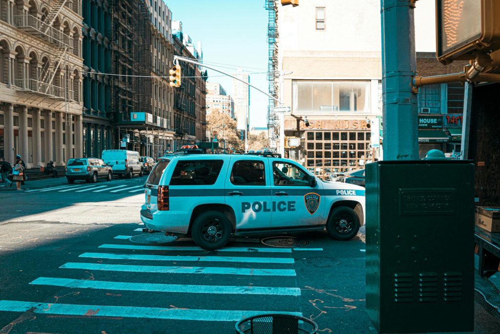 A police SUV at an urban intersection in New York City with pedestrians and traffic.