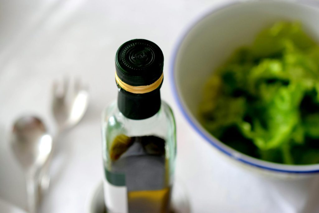 A high-angle view of an olive oil bottle alongside a fresh green salad and cutlery.