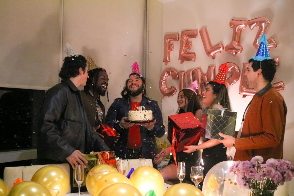 Group of friends celebrating a birthday with gifts and cake indoors.