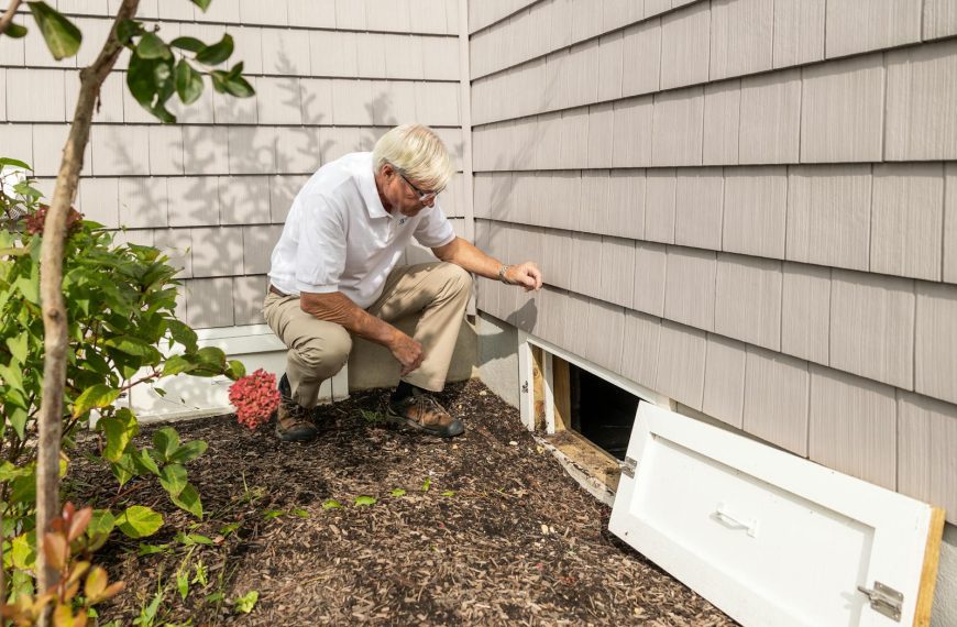 Senior adult inspecting a crawl space entrance during a home inspection on a sunny day.