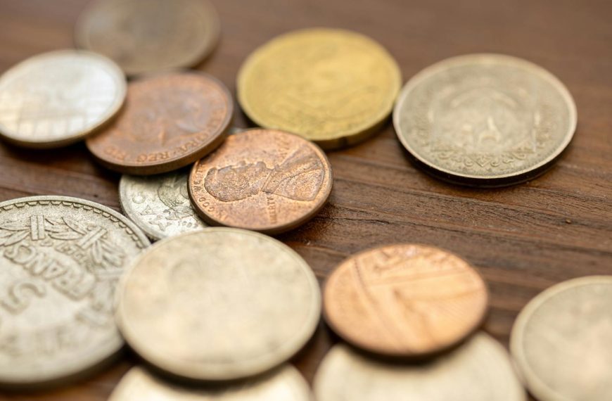 A detailed close-up image showing various vintage coins scattered on a wooden surface, capturing their unique textures and engravings.