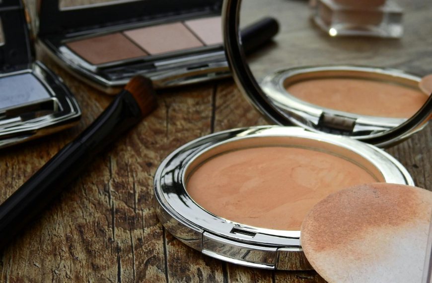 Close-up of makeup tools including compact, brush, and mirror on a rustic wooden surface.