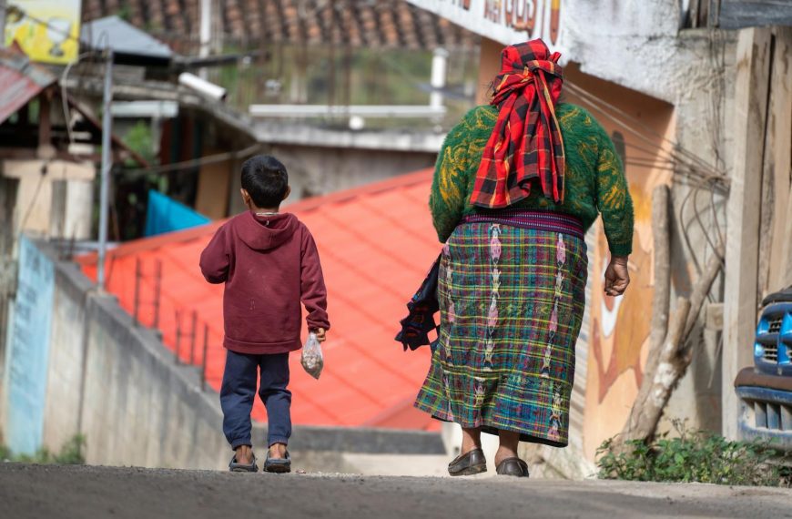 A Guatemalan woman and child walk down a street in Acul, Quiché, reflecting local culture and textiles.