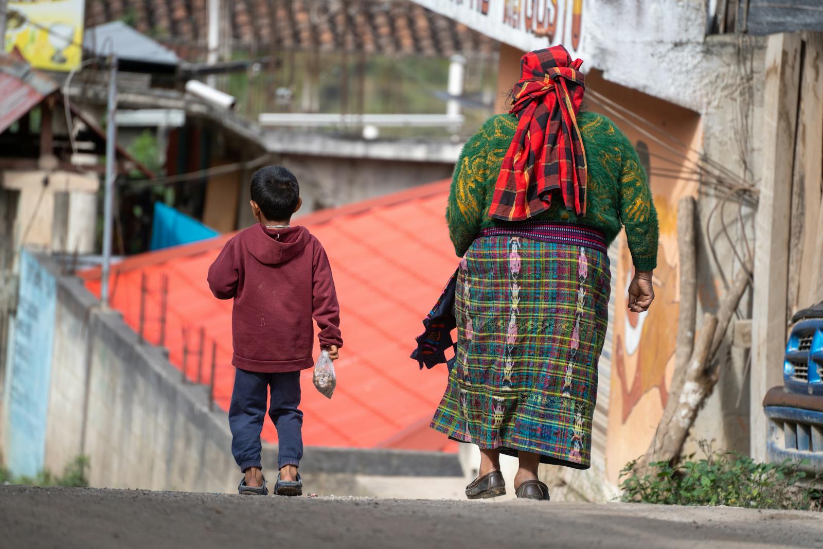 A Guatemalan woman and child walk down a street in Acul, Quiché, reflecting local culture and textiles.