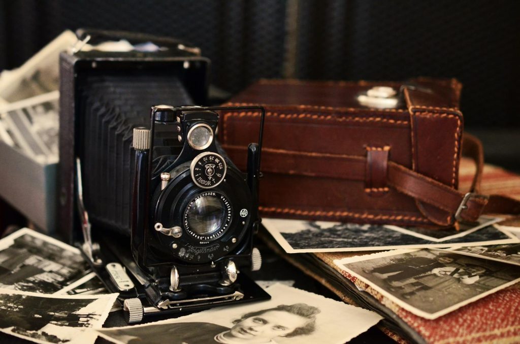Classic black vintage camera with old photographs and a leather case, displaying nostalgic charm.