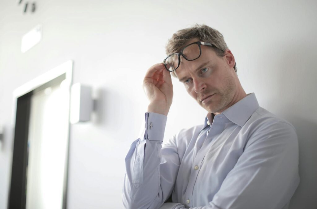 Thoughtful businessman adjusting glasses in a modern office setting, appearing pensive and focused.