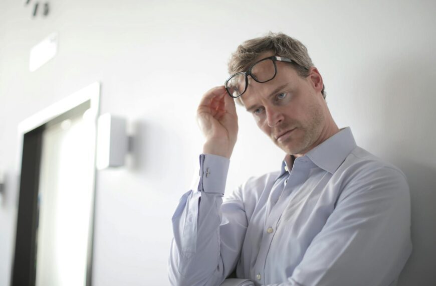 Thoughtful businessman adjusting glasses in a modern office setting, appearing pensive and focused.