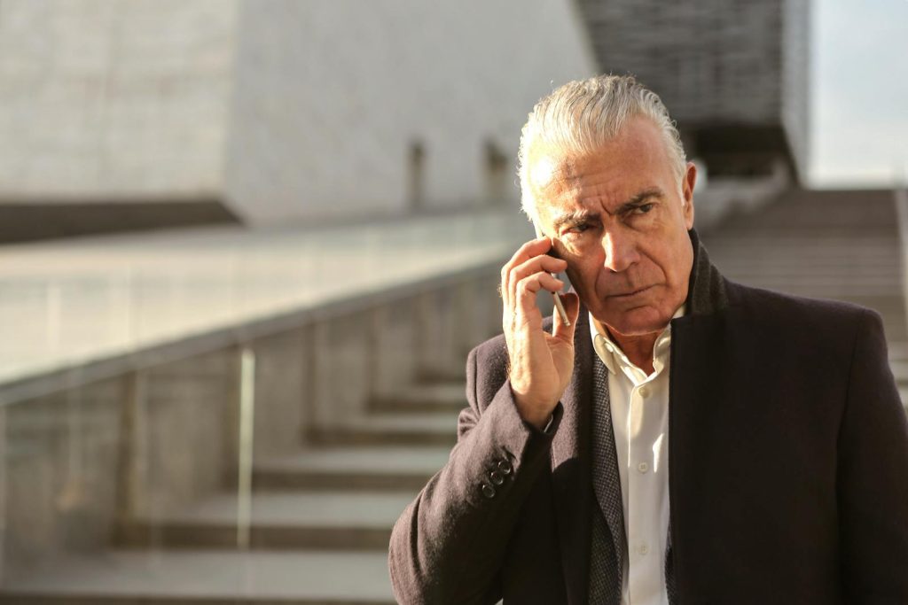 Serious senior businessman using a smartphone outdoors, conveying a professional and pensive mood.