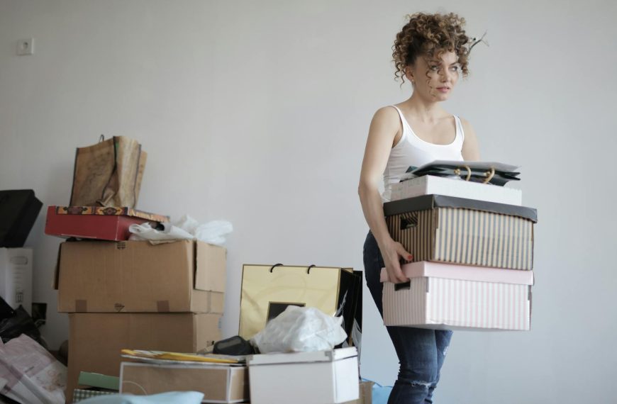 A young woman carrying boxes during a move into a new apartment, surrounded by packed belongings.