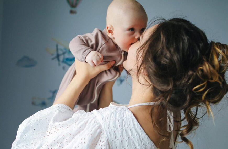 A heartwarming scene of a mother lovingly kissing her baby in a decorated room.