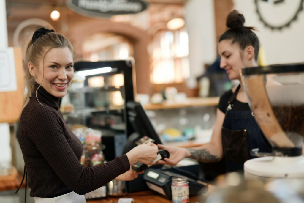 A smiling customer makes a contactless payment at a bustling café counter.